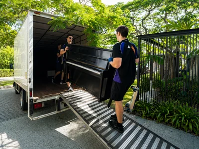 SwiftMove movers carrying a large dark cabinet on a truck ramp